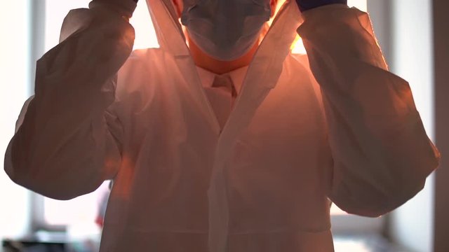 Scientist putting on medical suit and goggles, disposable protective coverall