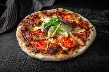 Tasty hot italian pizza with prosciutto, parmesan, arugula on black wooden table. Pizzeria menu. Concept poster for Restaurants or pizzerias