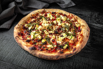 Tasty hot italian pizza with grape leaves, egg, meat on black wooden table. Pizzeria menu. Concept poster for Restaurants or pizzerias