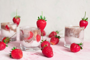 light strawberry dessert in a glass on a light background with fresh strawberries and cream and chocolate cream layers