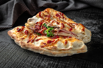 Tasty hot italian pizza calzone on black wooden table. Pizzeria menu. Concept poster for Restaurants or pizzerias