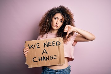 Young beautiful activist woman with curly hair and piercing protesting asking for a change with angry face, negative sign showing dislike with thumbs down, rejection concept