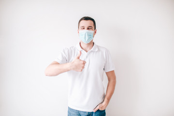 Young sick man isolated over white background. Guy in medical mask stand alone in studio and hold big thumb up. Protection from virus and flu.