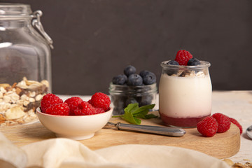 Breakfast with white yogurt with fresh raspberries and blueberries on the serving board on the rustic table.