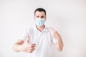 Young sick man isolated over white background. Guy wear facial medical mask for protection. Hold big thumb up. Protect himself from cold and virus.