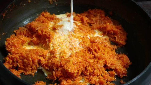 Addition of milk in pan with cooked grated carrot, preparation of Indian sweet or dessert, carrot halwa
