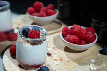 Morning yogurt breakfast with fresh raspberries, muesli and blueberries on a wooden board.