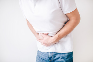 Young man isolated over white background. Cut view of guy holding hands over stomach because of diarrhea. Painful and aching.