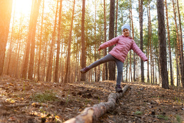 Young small cute adorable cheerful playful caucasian school girl enjoy having fun walking at spring or autumn forest balancing on log tree outdoor. Healthy outside nature family activity