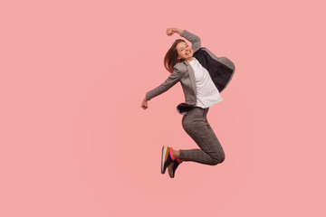 I'm champion! Portrait of enthusiastic ecstatic happy businesswoman in elegant suit jumping carefree in air, flying inspired by success, celebrating goal achievement. indoor studio shot isolated