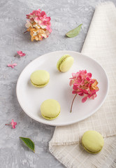 Green macarons or macaroons cakes on white ceramic plate on a gray concrete background  side view.