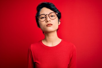 Fototapeta premium Young beautiful asian girl wearing casual t-shirt and glasses over isolated red background Relaxed with serious expression on face. Simple and natural looking at the camera.