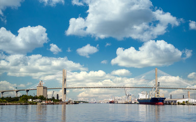 Fototapeta premium Freight industry at busy harbor on the Savannah River with suspension bridge