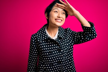 Young beautiful asian girl wearing casual jacket standing over isolated pink background very happy and smiling looking far away with hand over head. Searching concept.