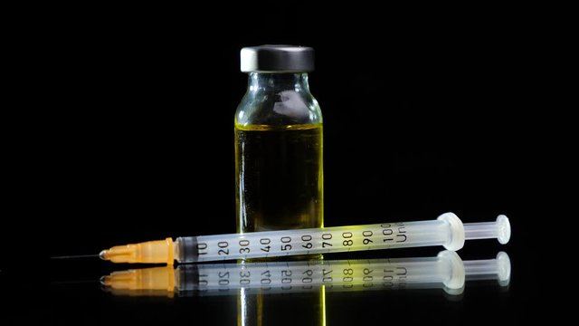 Glass vial filled with yellow liquid vaccine and insulin syringe rotate on a black background. Pharmaceutical industry. Viral infection treatment.