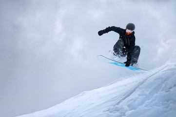 A professional snowboarder girl in flight after jumping from a snow eaves makes a rake against the...
