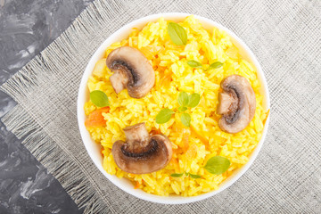 Yellow fried rice with champignons mushrooms, turmeric and oregano in white ceramic bowl on a black concrete background. top view.