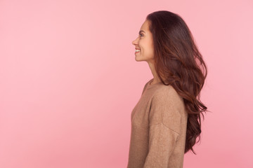 Side view of happy young woman with long brunette wavy hair smiling joyfully, expressing optimism,...