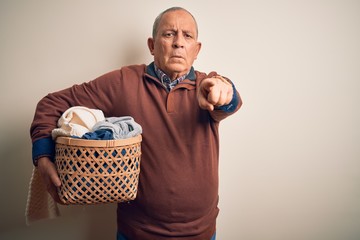 Senior handsome man holding wicker basket with clothes over isolated white background pointing with...