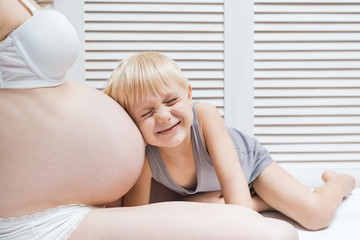 Funny little boy leaned his ear to belly of pregnant mother, closed his eyes and listens. Second pregnancy concept