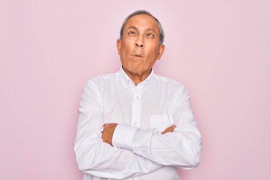 Senior handsome grey-haired man wearing elegant shirt over isolated pink background making fish face with lips, crazy and comical gesture. Funny expression.