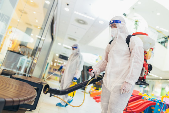 Professional workers in hazmat suits disinfecting indoor of mall, pandemic health risk, coronavirus