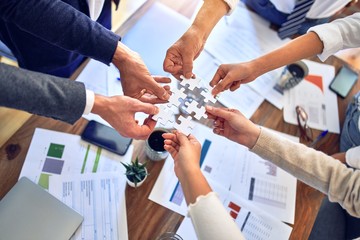 Group of business workers with hands together connecting pieces of puzzle at the office