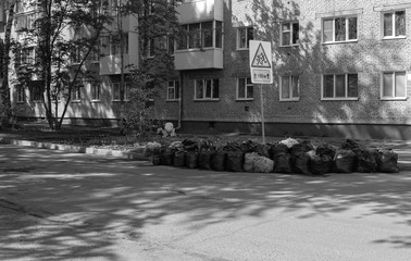 garbage bags on the background of houses where people live and a road sign
