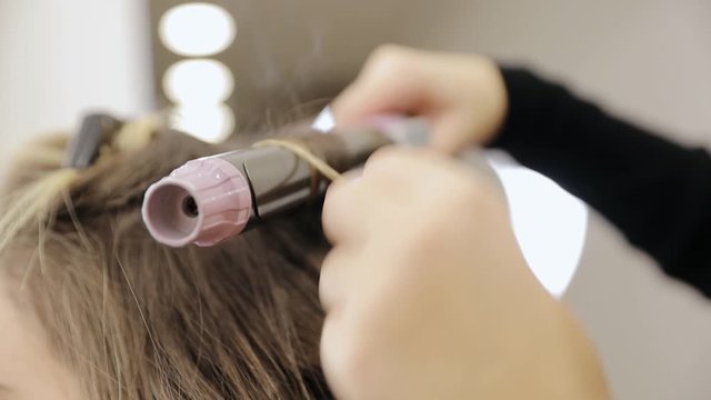 The hairdresser curls the hair with a styler and stacks them. Hairdresser-stylist makes the girl's hair. Close-up styler curls the hair