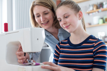 Mother Teaching Teenage Daughter How To Use Sewing Machine At Home