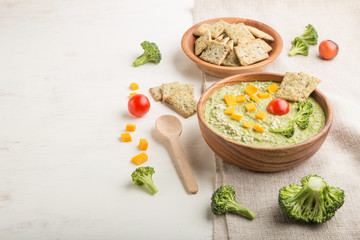 Green broccoli cream soup with crackers and cheese in wooden bowl on a white wooden background. side view, copy space.