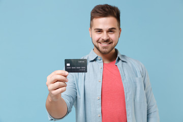 Smiling young bearded guy 20s in casual shirt posing isolated on pastel blue wall background studio portrait. People sincere emotions lifestyle concept. Mock up copy space. Hold credit bank card.