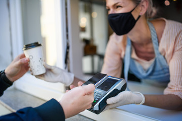 Woman with face mask serving coffee through window, shop open after lockdown.