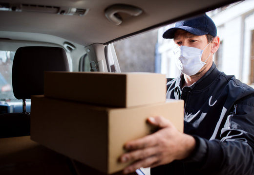 Delivery Man Courier With Face Mask Delivering Parcel Boxes In Town.