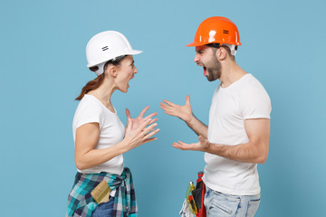 Angry irritated couple woman man in protective helmet hardhat isolated on blue background. Instruments accessories renovation apartment room. Repair home concept. Screaming swearing, spreading hands.
