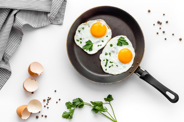 Fried eggs on frying pan on white desk top-down