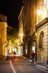 Fototapeta na wymiar Aix-en-Provence, France - Vue de nuit d'une rue de la vieille ville avec un passant qui marche et un scooter qui roule.