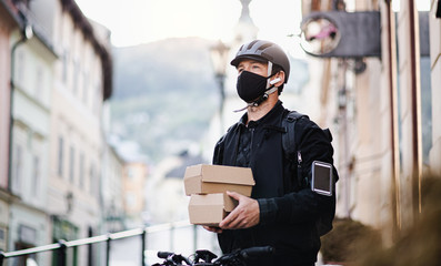 Delivery man courier with face mask and smartphone delivering parcel box in town.