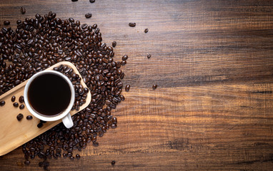 Black and brown coffee beans with cup of hot drink on  wooden table, top view copy space