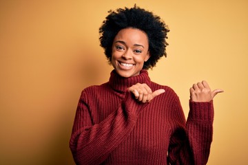 Young beautiful African American afro woman with curly hair wearing casual turtleneck sweater Pointing to the back behind with hand and thumbs up, smiling confident