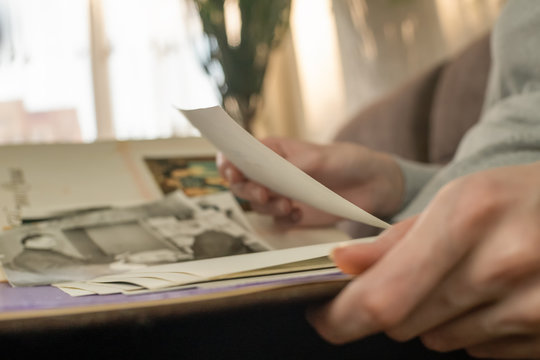 young woman holds an old photo album on her lap and looks at black and white photos, close up