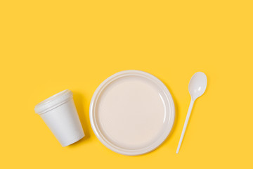 Plato redondo blanco, vaso y cuchara de plástico desechable sobre fondo amarillo liso brillante y aislado. Vista superior. Copy space