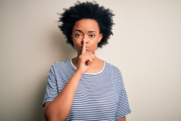 Fototapeta na wymiar Young beautiful African American afro woman with curly hair wearing striped t-shirt asking to be quiet with finger on lips. Silence and secret concept.