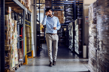 Full length of young businessman walking around warehouse and having headache.