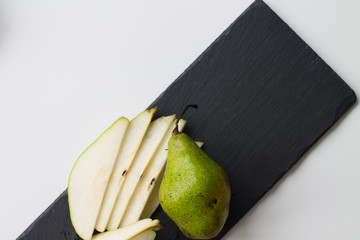 pears on a slate board, a white table and a wall of wood.