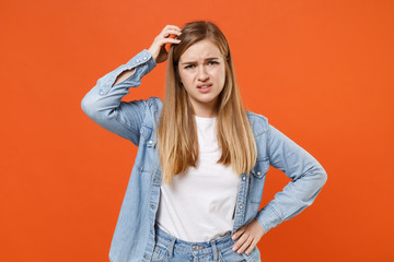 Preoccupied young woman girl in casual denim clothes posing isolated on bright orange wall background studio portrait. People sincere emotions lifestyle concept. Mock up copy space. Put hand on head.