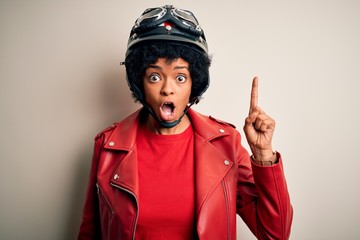 Young African American afro motorcyclist woman with curly hair wearing motorcycle helmet pointing finger up with successful idea. Exited and happy. Number one.