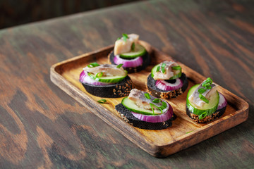 Smorrebrod, tapas or sandwich with onion, cucumber and herring  on the cutting board.  Copy space