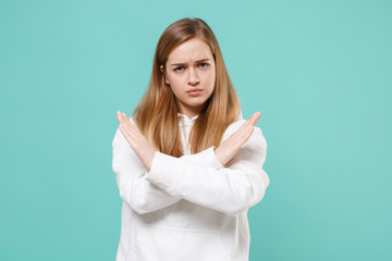 Displeased young woman girl in casual white hoodie posing isolated on blue turquoise background studio portrait. People lifestyle concept. Mock up copy space. Showing stop gesture with crossed hands.