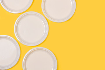 Platos redondos blanco de plástico desechable sobre fondo amarillo liso brillante y aislado. Vista superior. Copy space. Patón
